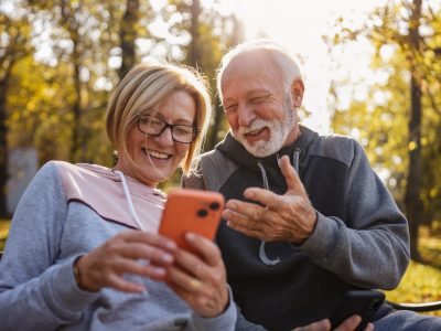 Eine ältere Frau und ein älterer Mann blicken auf ein Smartphone.