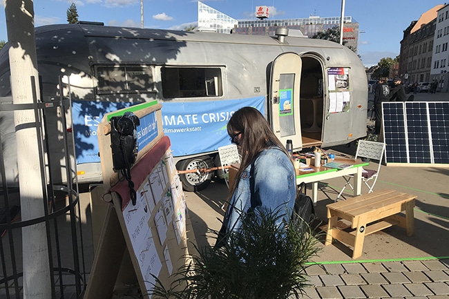 Eine Frau steht vor einem Camper und schaut sich eine Tafel an.