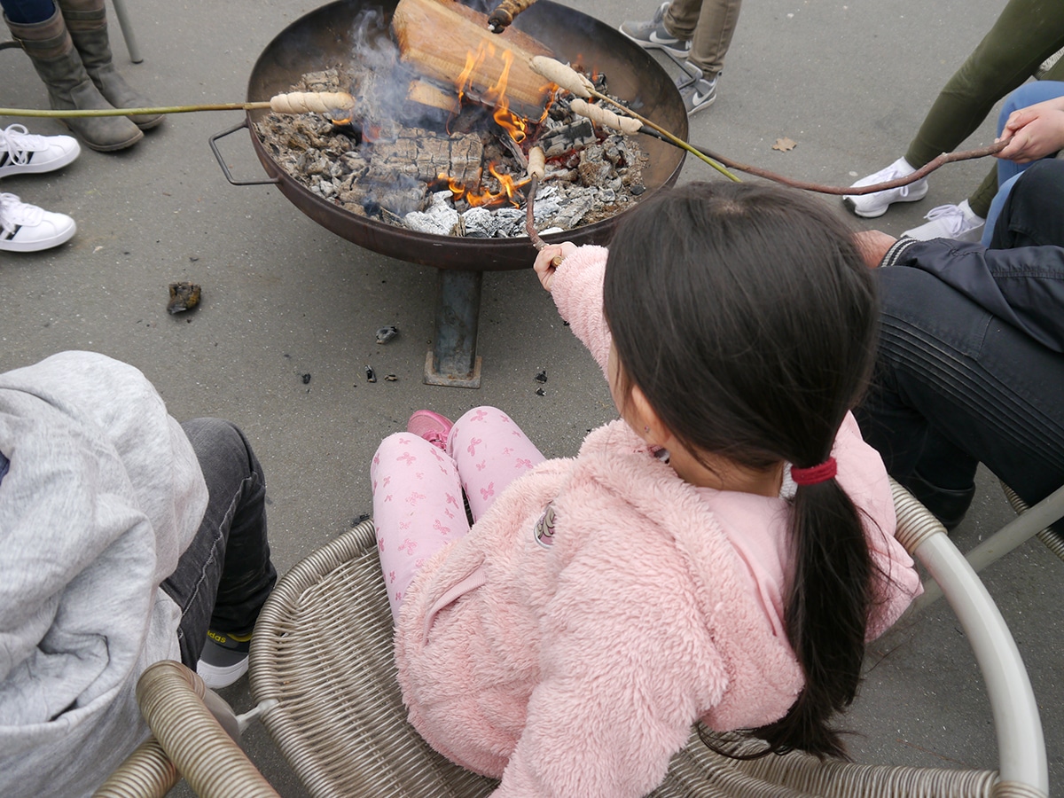 Kinder sitzen vor einer Feuerschale und backen Stockbrot
