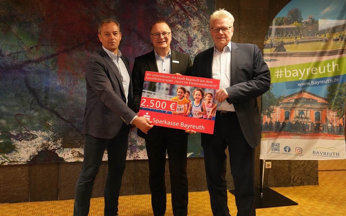 Drei Männer halten einen übergroßen Scheck in die Kamera.
