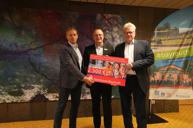 Drei Männer halten einen übergroßen Scheck in die Kamera.