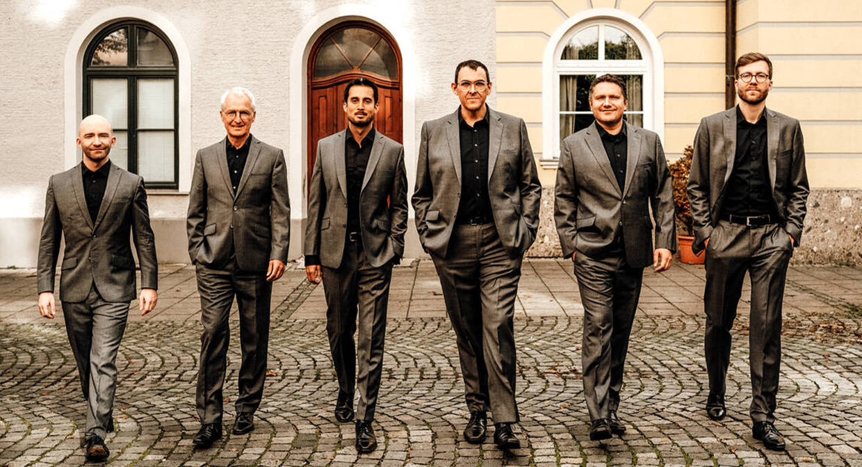 Sechs Männer in grauen Anzügen stehen vor einer Hauswand. | Foto: Dora Drexel