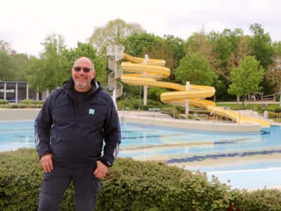 Mann steht vor dem Schwimmbecken, im Hintergrund die große Wasserrutsche