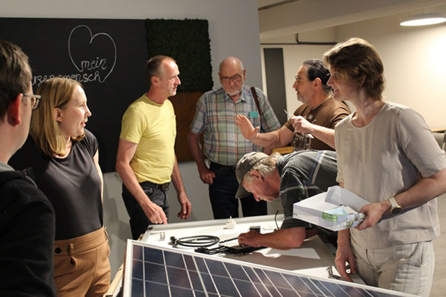 Teilnehmende des ersten Workshops am 15. Mai erkundigen sich bei Rupert Paintmayer (Mitte, gelbes T-Shirt) über technische Details zu Wechselrichter und Verkabelung.