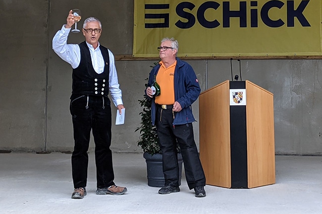 Zwei Handwerker stehen mit Wein in der Hand, der Zinmmerer hebt das Weinglas zum Richtspruch