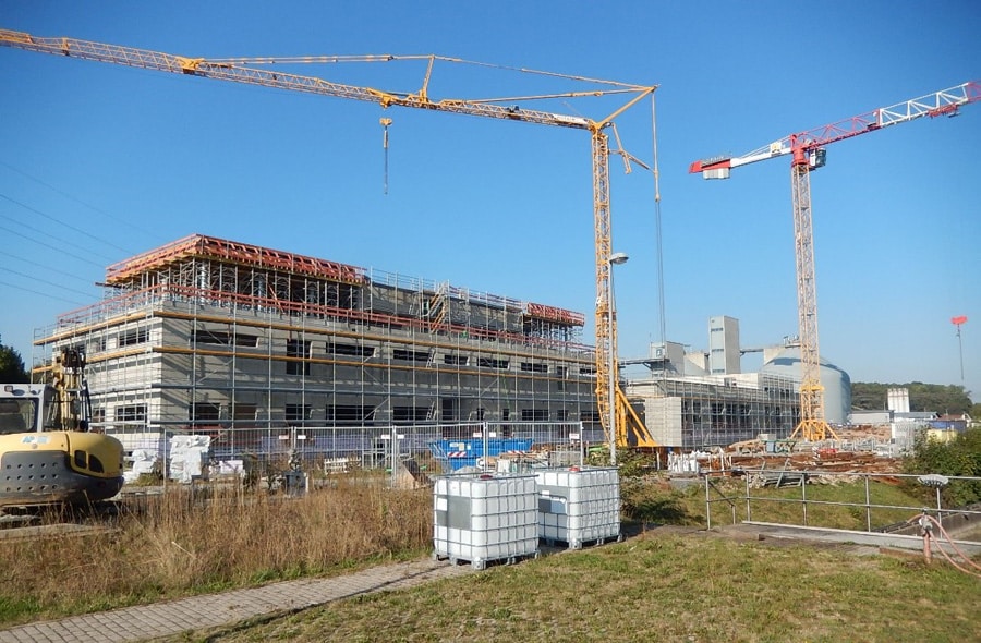 Ein Gerüst an allen Außenwänden des fertigen Rohbaus. Im Vordergrund zwei Kräne.