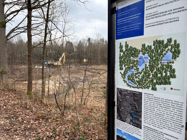 Die Baustelle für die rekultivierten Teiche im Studentenwald. Im Vordergrund ist eine Infotafel zu sehen, im Hintergrund ein Bagger.
