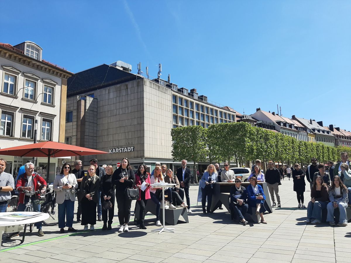 Mehrere Menschen sitzen auf den Sitztreppen, im Hintergund das Karstadtgebäude und der Baumsaal