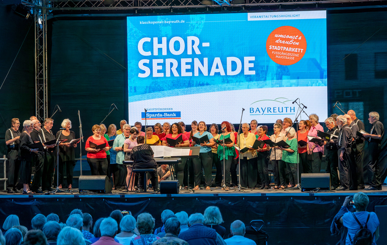 Ein Chor singt auf einer beleuchteten Bühne vor Publikum. | Foto: Stadt Bayreuth