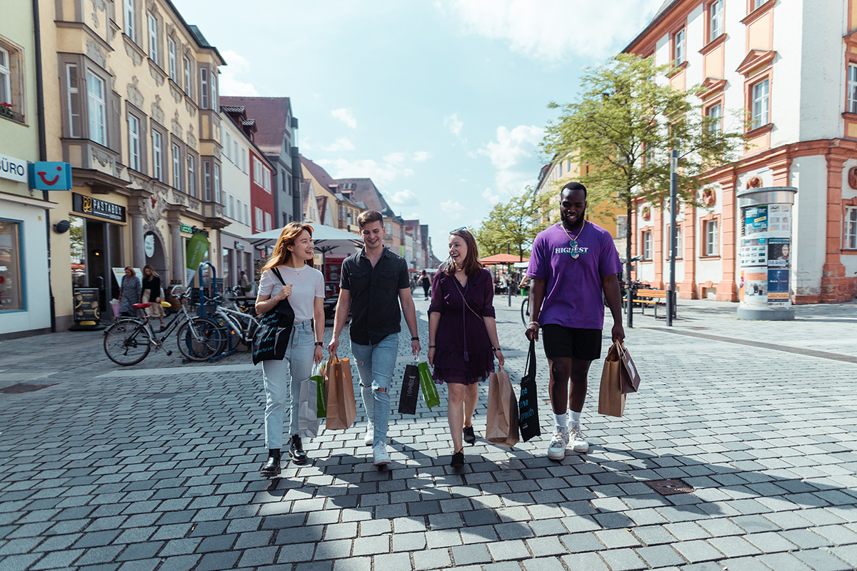 4 Leute schlendern mit Einkaufstüten durch die Innenstadt