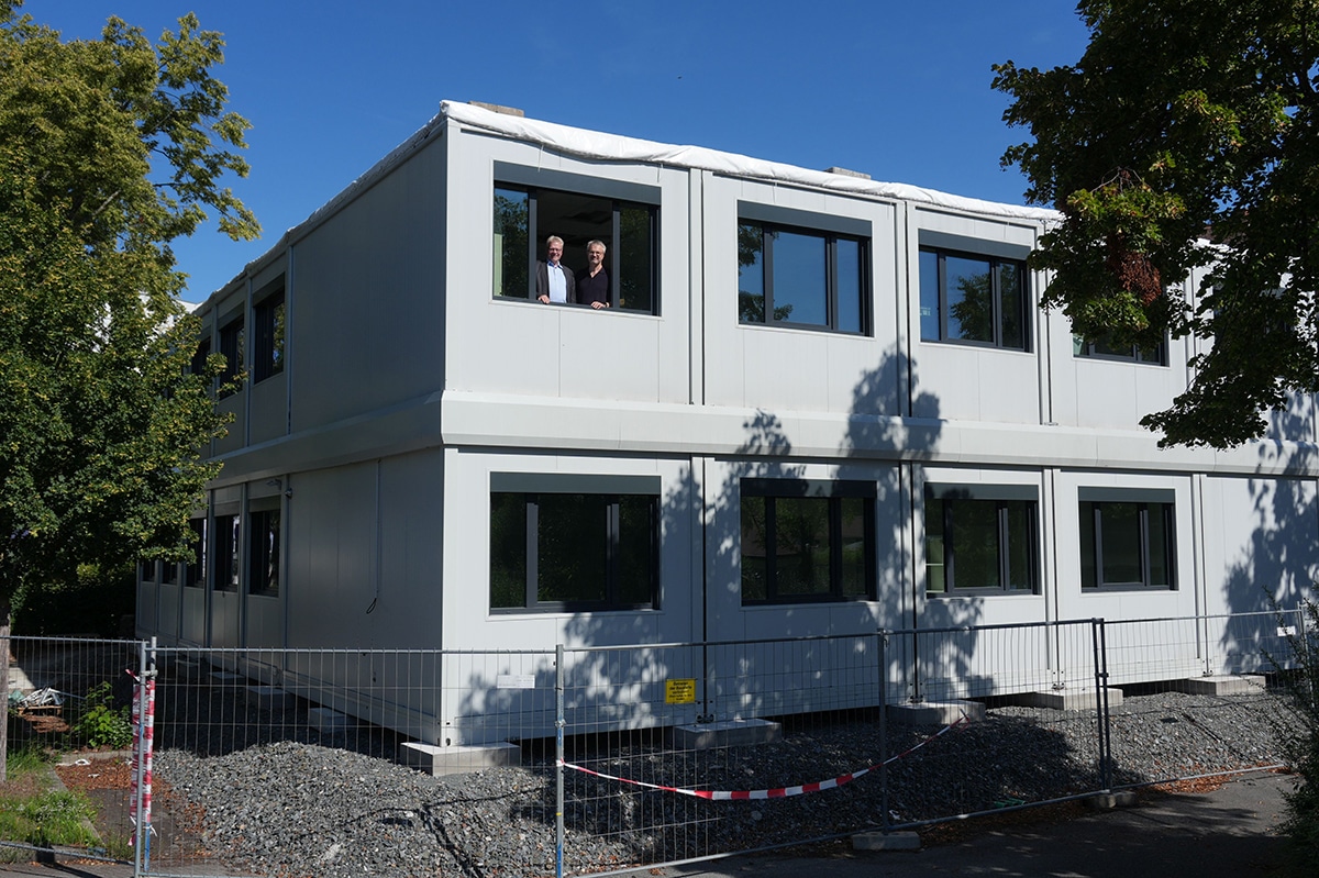 Das modulare Unterrichtsgebäude von außen, im 1. Stock schauen OB und Schulleiter aus dem Fenster