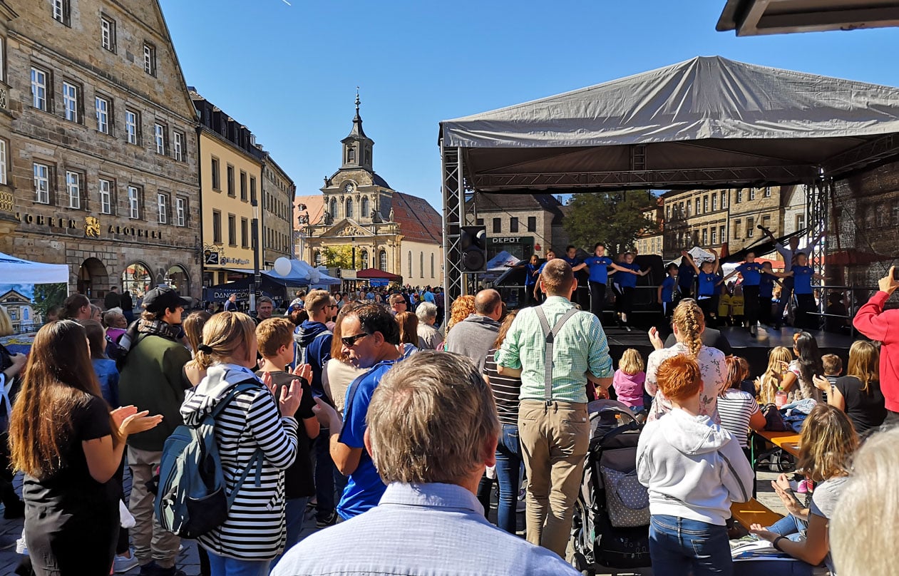 Zahlreiche Menschen stehen vor einer Veranstaltungsbühne mit Kindern. | Foto: BMTG