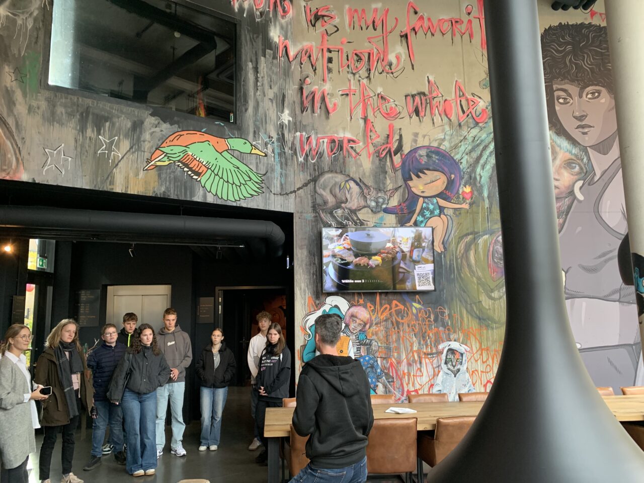 Eine Gruppe steht im Foyer des Hotels. An den Wänden sieht man zahlreiche Garffitis