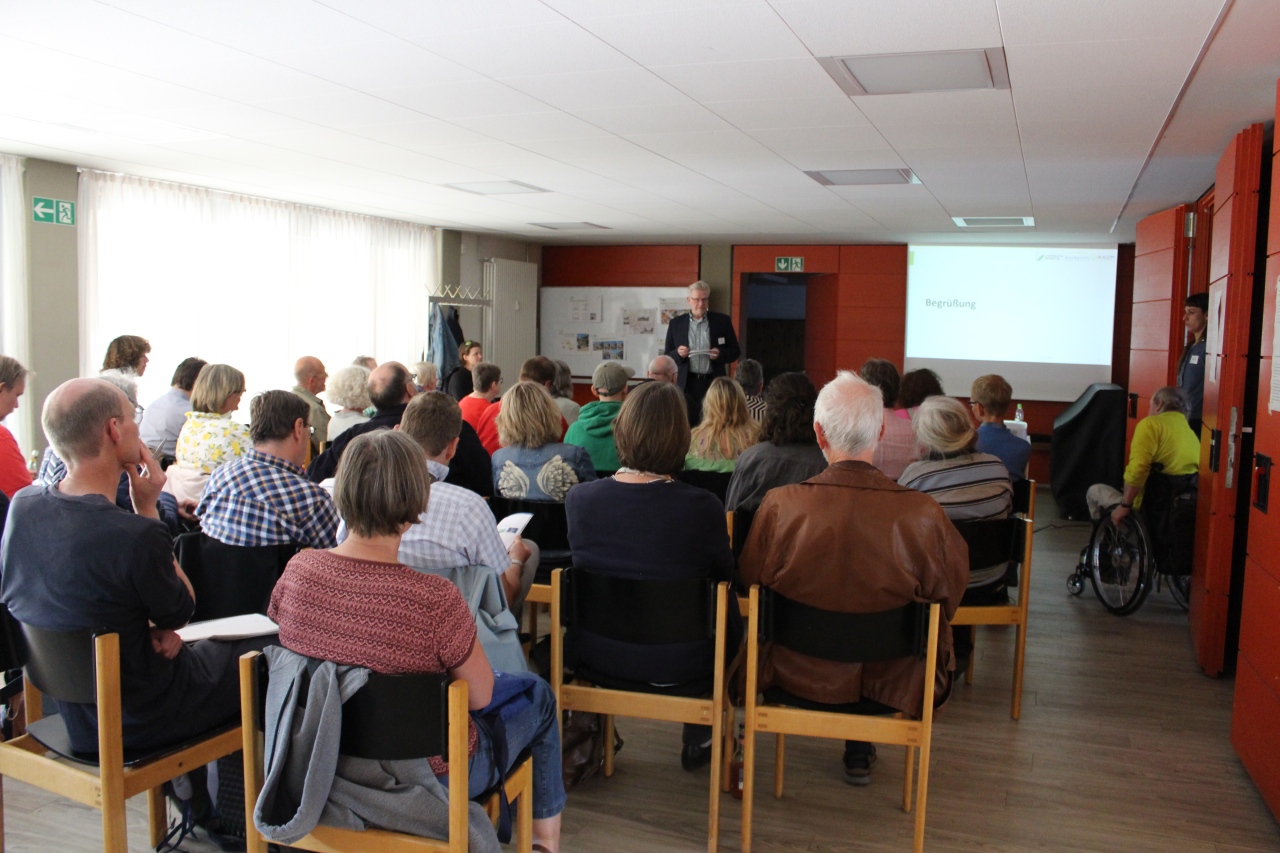 Menschen sitzen auf Stühlen in einem Besprechungsraum und hören den Worten des Oberbürgermeisters Thomas Ebersberger zu, welcher die Begrüßungsrede hält.