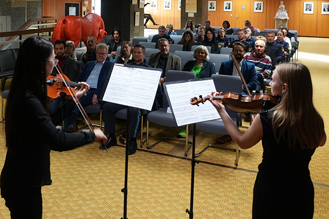 Im Vordergrund stehen zwei Violinistinnen und dahinter sitzen die Zuhörer.