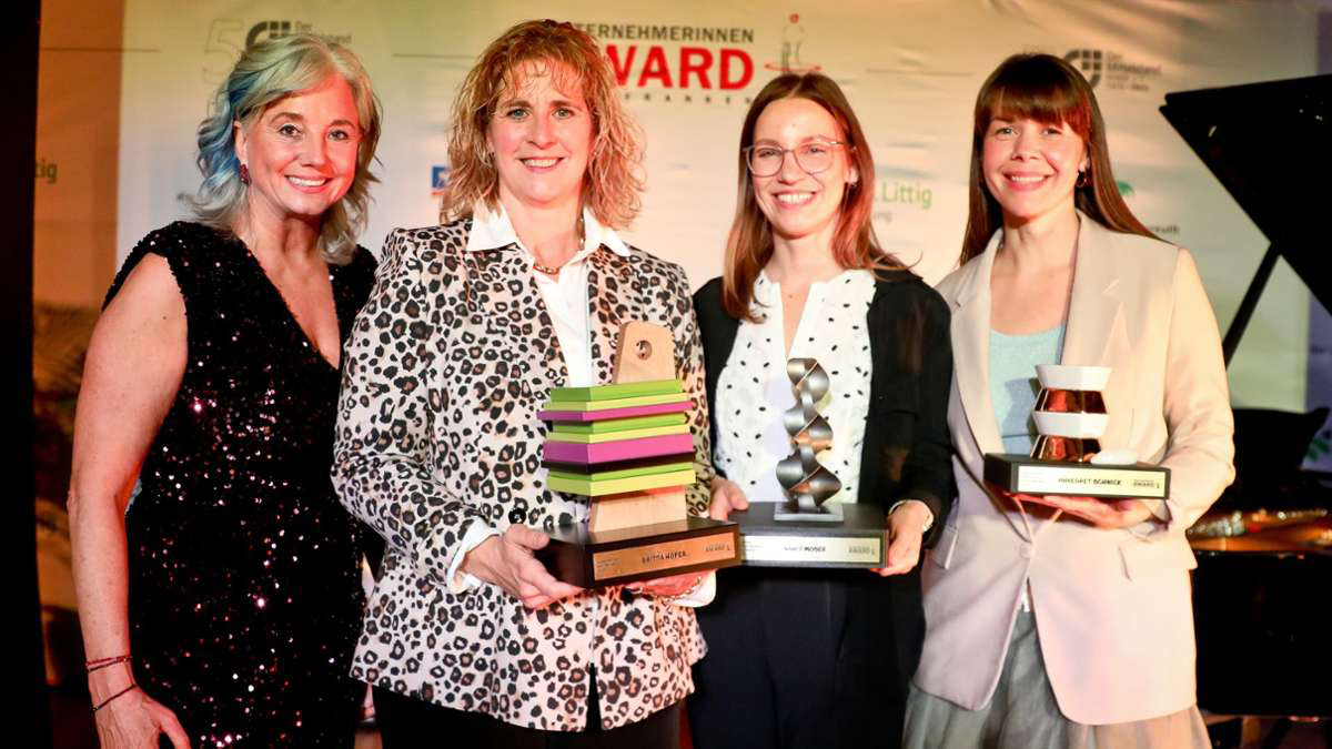 4 Frauen stehen nebeneinander, lächeln und halten Trophäen in den Händen