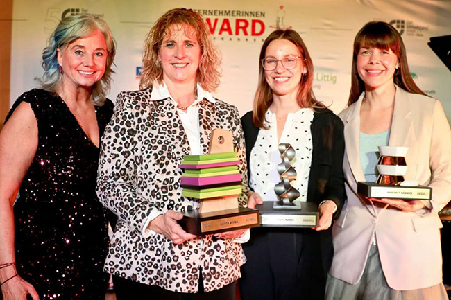 4 Frauen stehen nebeneinander, lächeln und halten Trophäen in den Händen