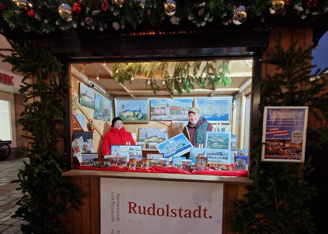 Eine Frau und ein Mann präsentieren in einer Weihnachtsbude Bilder. | Foto: Stadt Bayreuth