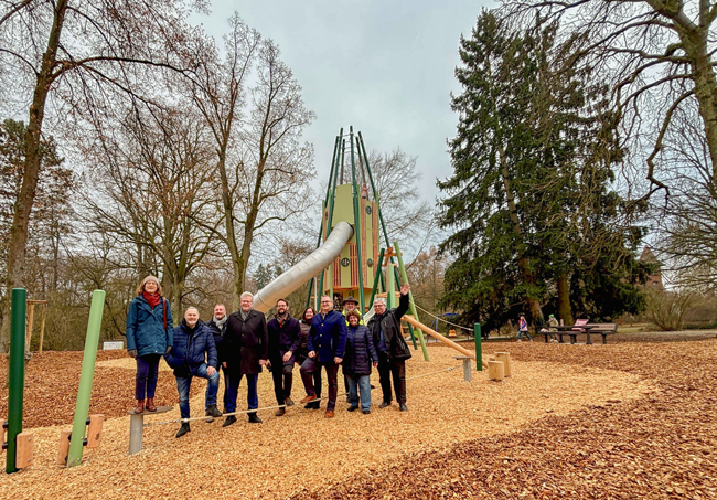 Eine Personengruppe steht vor einem Spielgerät auf einem herbstlichen Spielplatz. Foto: Stadt Bayreuth
