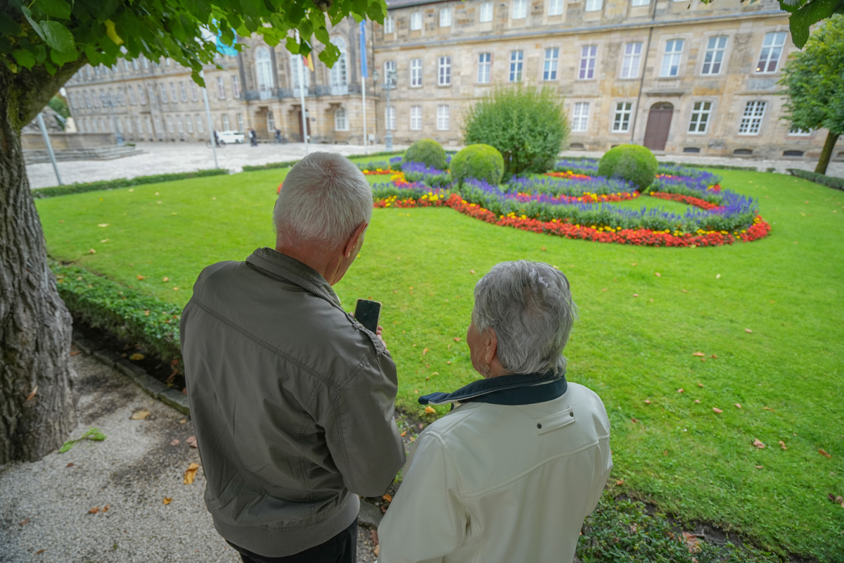 Ein älteres Ehepaar beim Neuen Schloss mit Blick auf ein Smartphone bzw. Handy. Foto: Stadt Bayreuth