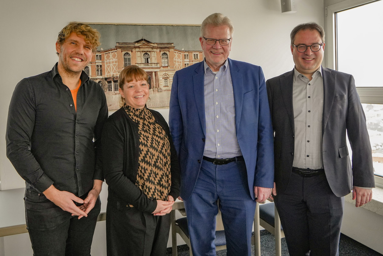 Drei Männer und eine Frau stehen vor einer Abbildung des Bayreuther Festspielhauses. | Foto: Stadt Bayreuth
