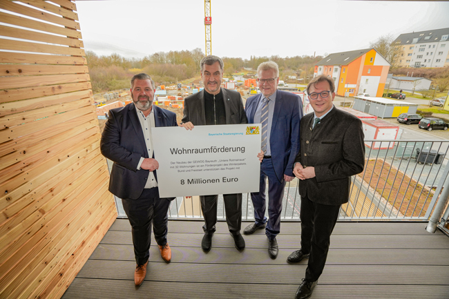 Vier Männer stehen auf einem Balkon und halten eine Förderbescheid in die Höhe: (v. li.) GEWOG-Geschäftsführer Jürgen Kastner, Ministerpräsident Dr. Markus Söder, der Aufsichtsratsvorsitzende der GEWOG, Oberbürgermeister Thomas Ebersberger und MdL Franc Dierl. Foto: Stadt Bayreuth