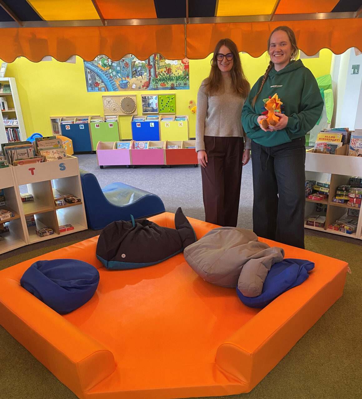 Kathrin Weishäupl (li.) von Miss Smarthead GmbH übergibt das Kuschelnest an Kinderbibliotheksleitung Alexandra Warzecha. Foto: RW21 Stadtbibliothek