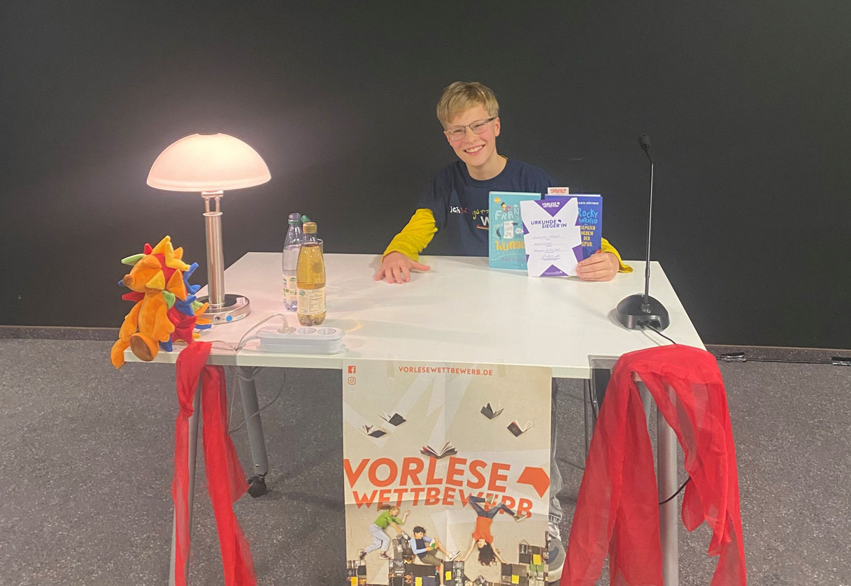 Ein Junge sitzt hinter einem Tisch und präsentiert ein Buch.