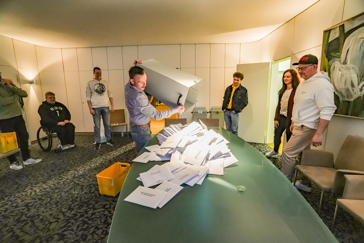 Ein Wahlhelfer entleert im Beisein von mehreren Wahlhelferinnen und -helfern eine Wahlurne auf einem Tisch. Foto: Stadt Bayreuth