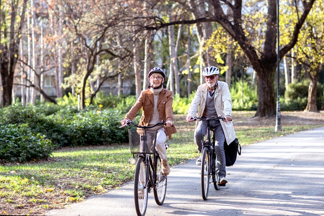 Zwei Senioren fahren mit Fahrrädern durch einen Park. Foto: Adobe Stock