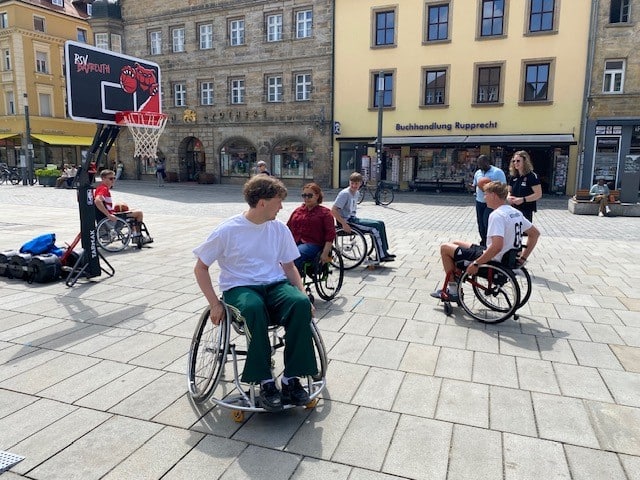 Menschen spielen im Rollstuhl sitzend Basketball auf dem Stadtparkett