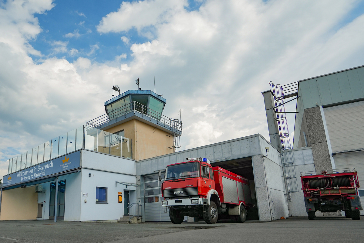 Das Hauptgebäude mit Tower des Verkehrslandeplatzes Bayreuth – hier wurden fast 13.500 Flugzeugbewegungen in 2025 gezählt. Für den Brandschutz ist mit einem speziellen Feuerwehrfahrzeug gesorgt. Die Aussichtsplattform unterhalb des Towers ist für Besucher übrigens jederzeit frei zugänglich, um den Flugbetrieb zu verfolgen. Foto: Stadt Bayreuth