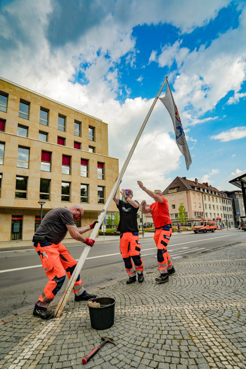 Drei Mitarbeiter des Stadtbauhofs stellen am Luitpoldplatz einen Fahnenmast auf. Foto: Stadt Bayreuth