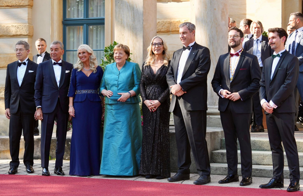Ministerpräsident Söder, die ehemalige Bundeskanzlerin Merkel, OB Zippel, Festspielleiterin Katharina Wagner und weitere Personen stehen vor dem Eingang ins Festspielhaus. | Foto: Stadt Bayreuth