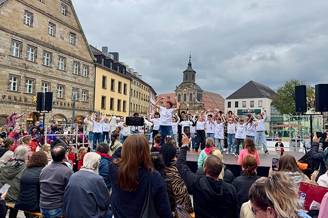 Menschen auf dem Stadtparkett, die einer Gruppe auf der Bühne zuhören.