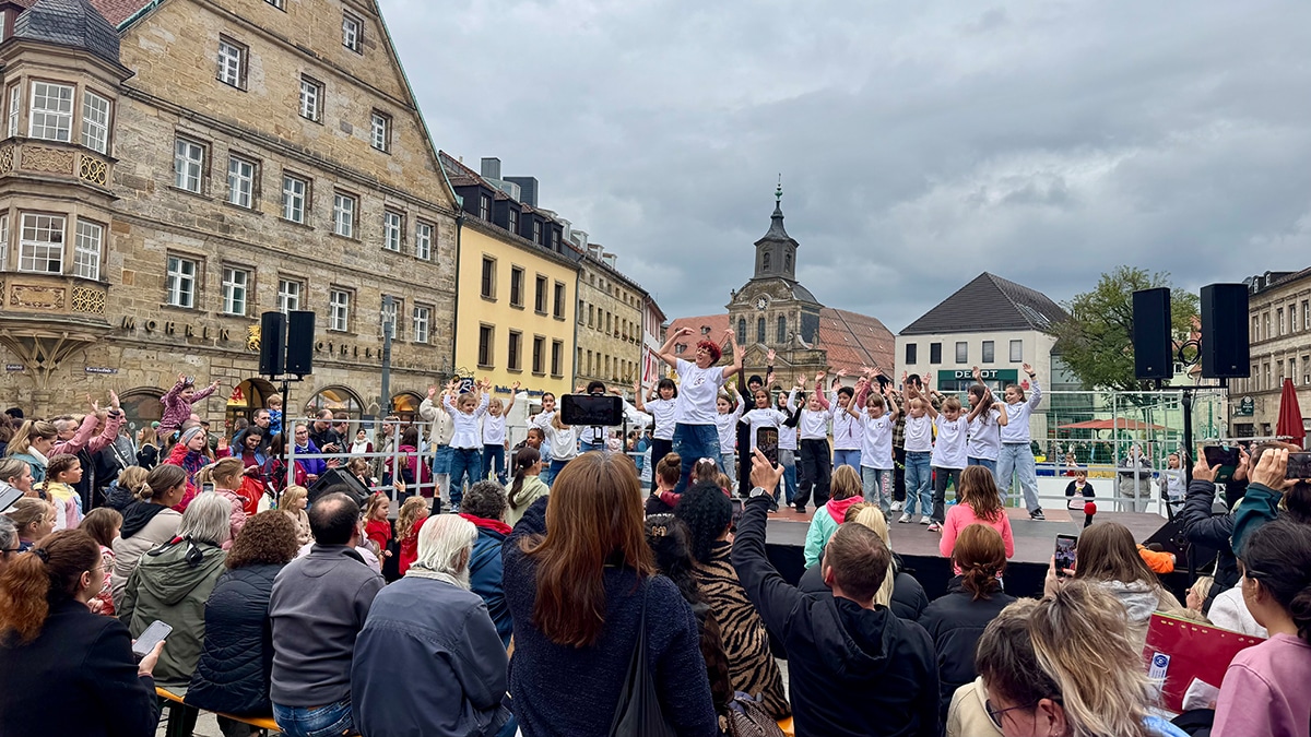 Menschen auf dem Stadtparkett, die einer Gruppe auf der Bühne zuhören.