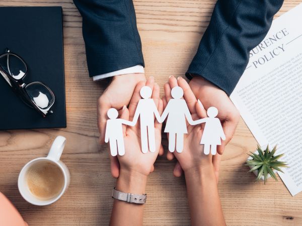 Ein Mann und eine Frau halten ihre Hände ausgestreckt aufeinander und halten gemeinsam eine Familie aus Papier in der Hand