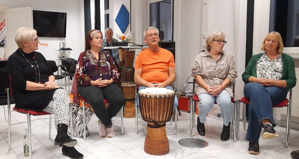 Fünf Menschen sitzen auf Stühlen, vor ihnen steht eine Pauke